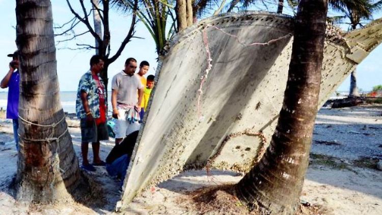Fischer begutachten das Wrackteil an seinem Fundort an einem Strand in Südthailand.