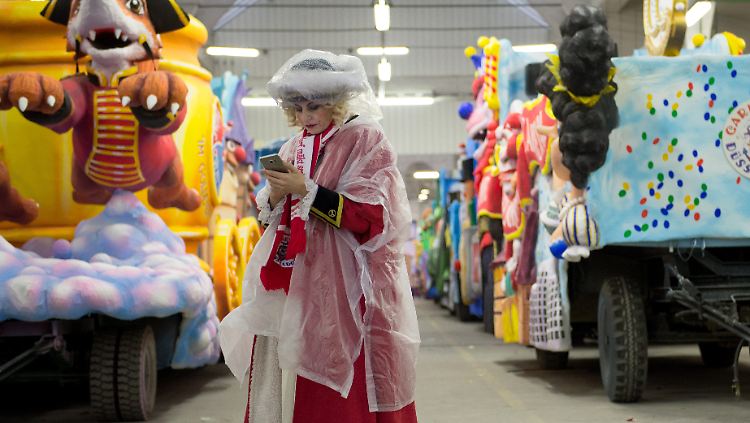 Wie wird das Wetter am 13. März? Eine verkleidete Karnevalistin im Regenschutz schaut im Depot des Düsseldorfer Festumzugs auf ihr Handy.