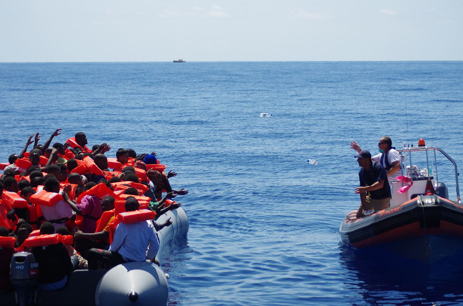 Helfer werfen Flüchtlingen auf See Wasserflaschen zu: Den Menschen fehlt während ihrer Flucht übers Mittelmeer in der Regel alles - auch Nahrung und ausreichend zu trinken.  