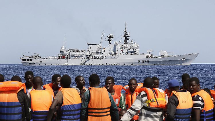 Flüchtlinge warten auf einem Schlauchboot darauf, von einem italienischen Zerstörer aufgesammelt zu werden.