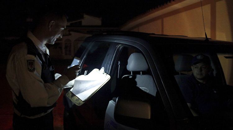 Ein Polizist muss für eine Verkehrskontrolle das Licht seines Handys benutzen. Die Straßenbeleuchtung wurde bereits vor Wochen abgestellt.