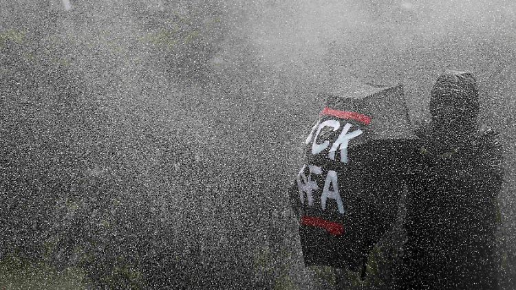 Ein Teilnehmer der rechten Demonstration versucht, sich gegen die Wasserwerfer zu schützen.