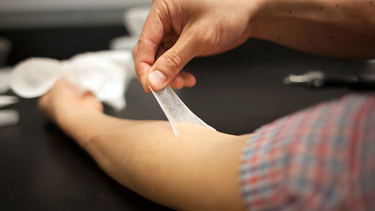 Eine künstliche zweite Haut aus Silikon wird von einem Arm abgezogen. Die dünne Schicht aus Silikon-Polymeren mindert Alterserscheinungen sichtbar - vorübergehend.