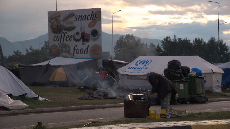 Unter einer Werbetafel an der Autobahn bereitet eine alte Frau Essen zu.