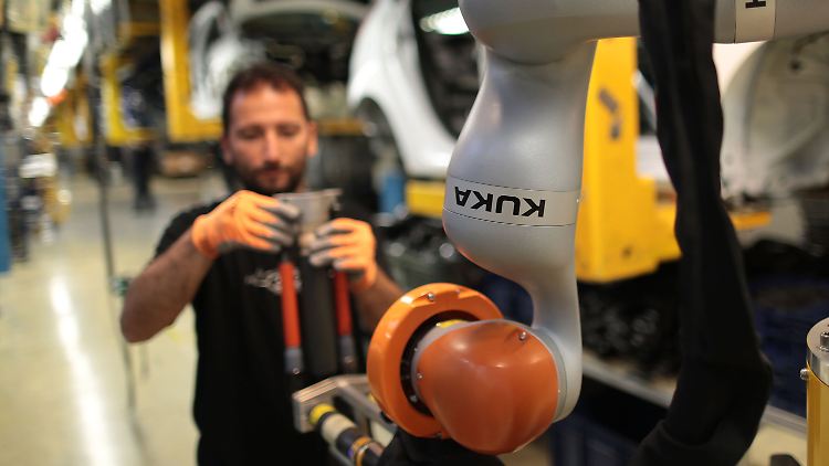 Ein Ford-Mitarbeiter montiert mit einem Kuka-Roboter einen Stoßdämpfer.