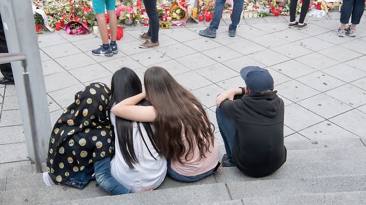 Mädchen sitzen vor dem Olympia-Einkaufszentrum in München, wo Blumen und Kerzen an die Opfer des Amoklaufs erinnern.