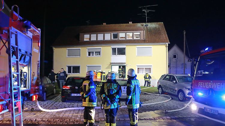 Einsatzkräfte der Feuerwehr stehen vor dem Haus, in dem das Feuer gelegt worden ist.