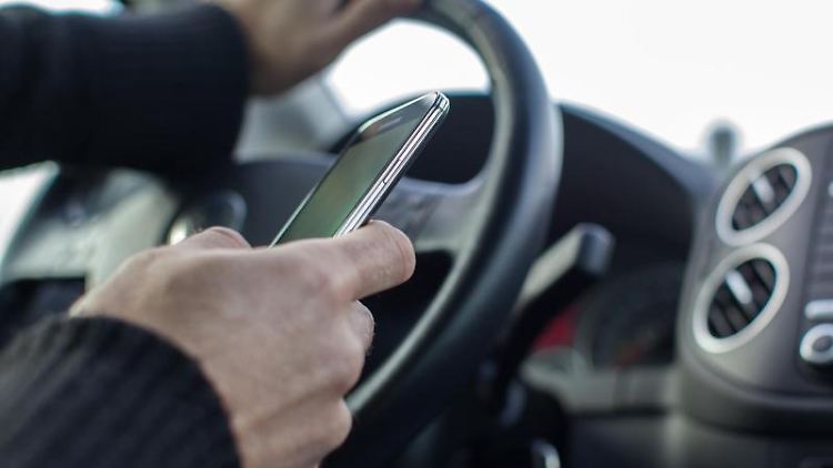 Autofahrer mit Handy am Steuer.