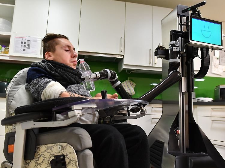 Sascha Dohrn bedient mit einer Mundsteuerung Roboter Marvin, der ihm eine Flasche Wasser reichen soll.