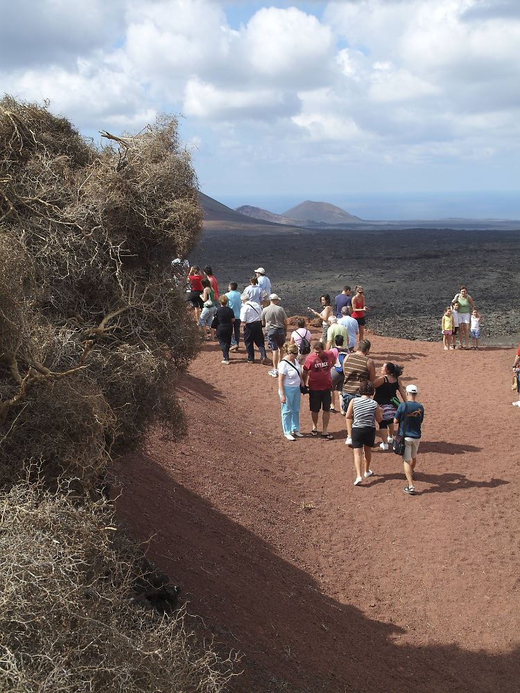 Touristen wandern durch die Landschaft der Feuerberge des Timanfaya-Nationalparks auf Lanzarote.