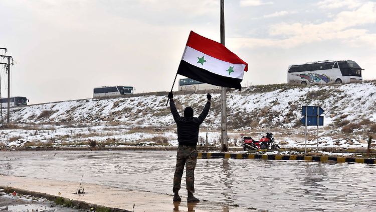 Ein Mann schwenkt die syrische Flagge, während Busse Rebellen aus Aleppo bringen.