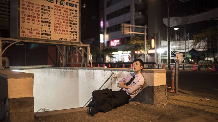Ein junger Mann mit Anzug und Krawatte schläft vor Erschöpfung im Tokioter Stadtteil Asakusa an einer U-Bahn-Station ein.
