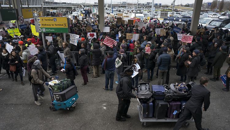 Reisende passieren am New Yorker Flughafen John F. Kennedy Demonstranten, die gegen den Einreisestopp protestieren.