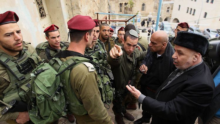 Palästinensische Männer diskutieren auf einer Straße in Hebron mit israelischen Soldaten über den Zugang zu ihrem Land.