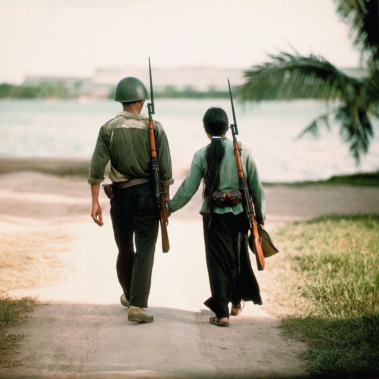 Zwei junge Vietnamesen gehen Hand in Hand einen Weg entlang. Es könnte ein idyllisches Foto sein - wären da nicht die Gewehre, die beiden griffbereit über der Schulter hängen.