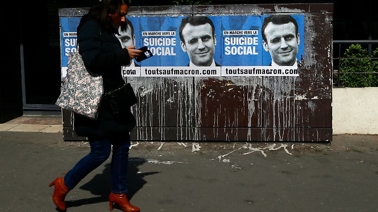 Eine Frau läuft in Paris an einem Wahlplakat vorbei, das sich gegen Emmanuel Macron richtet.