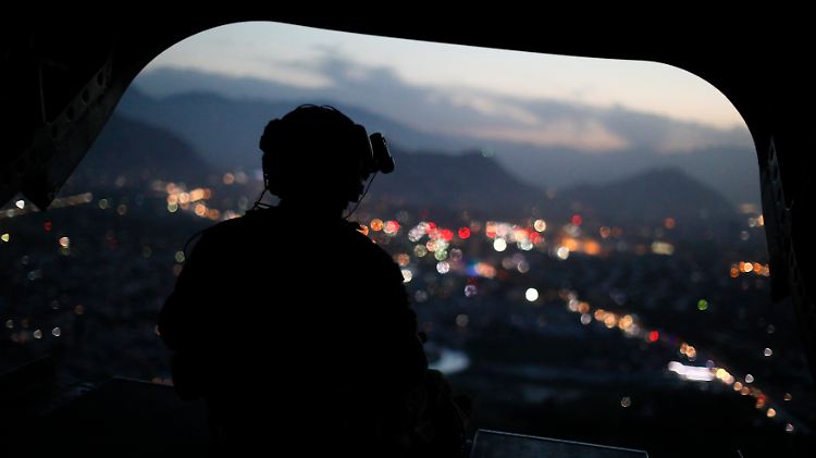 Ein US-Soldat beobachtet aus der Heckklappe eines Hubschraubers heraus die Lichter des abendlichen Kabul.