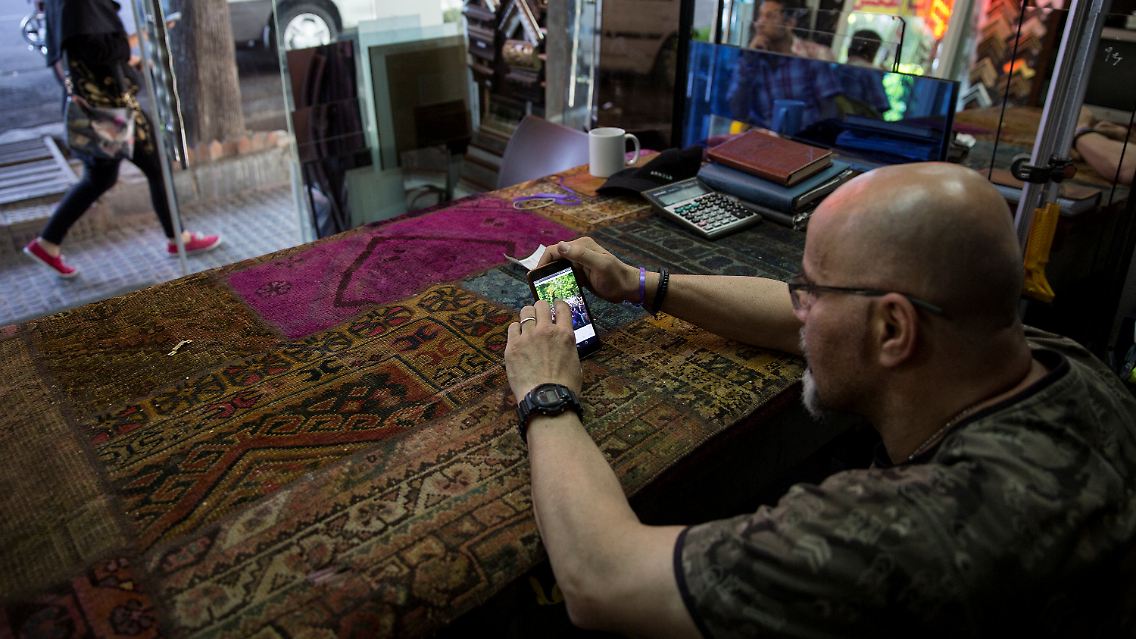 Ein Mann liest in seinem Geschäft in Teheran auf seinem Smartphone. Am Freitag wird im Iran ein neuer Präsident gewählt.