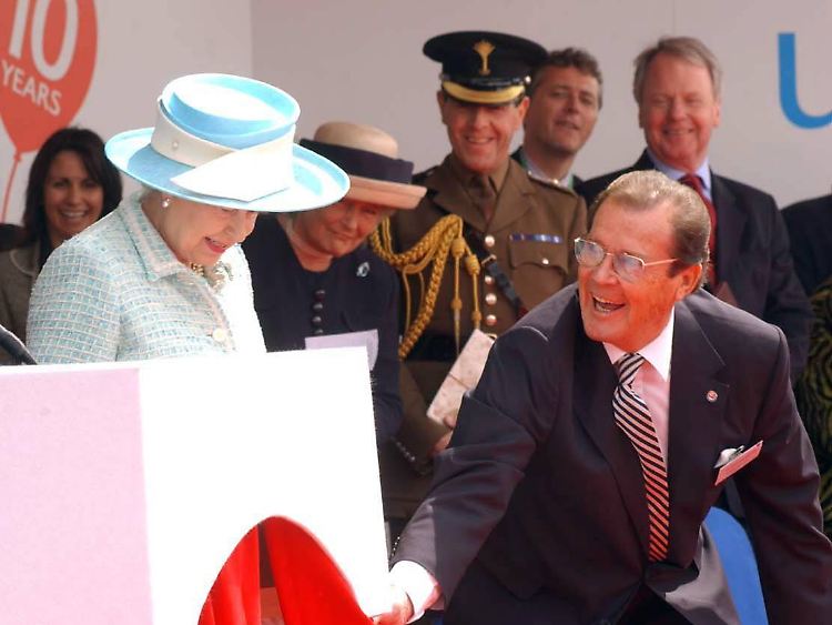 Roger Moore bringt selbst die Queen zum Lächeln - bei einer Veranstaltung 2005 half er der Königin vom Podium.