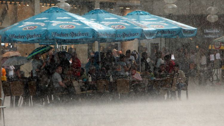 Ein wirklich verregneter Café-Besuch: Auf dem Münchner Marienplatz suchen Passanten vor dem Starkregen Schutz unter den Schirmen einer Gaststätte.