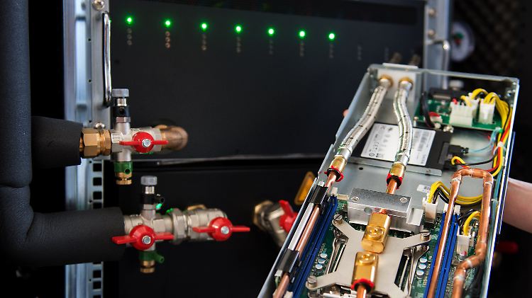 Eine Mitarbeiterin der Cloud & Heat Technologies GmbH, Nicolas Röhrs, hält ein durch Wasser gekühltes Servermodul vor einem Server in den Händen.