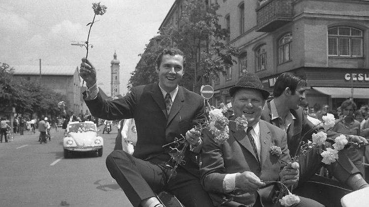 Beckenbauer grüßt mit Nelke, vorher zeigt er dem "verehrten Publikum" eine weniger charmante Geste.