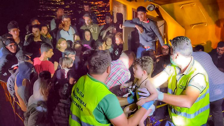 Grenzpolizisten heben im Hafen von Constanta ein Kind aus dem Flüchtlingsboot.