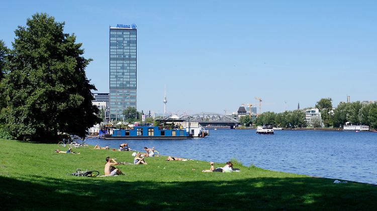 Wiese im Treptower Park an der Spree, neben Hausbooten und Dampferanlegestelle - am Horizont sieht man den Fernsehturm.