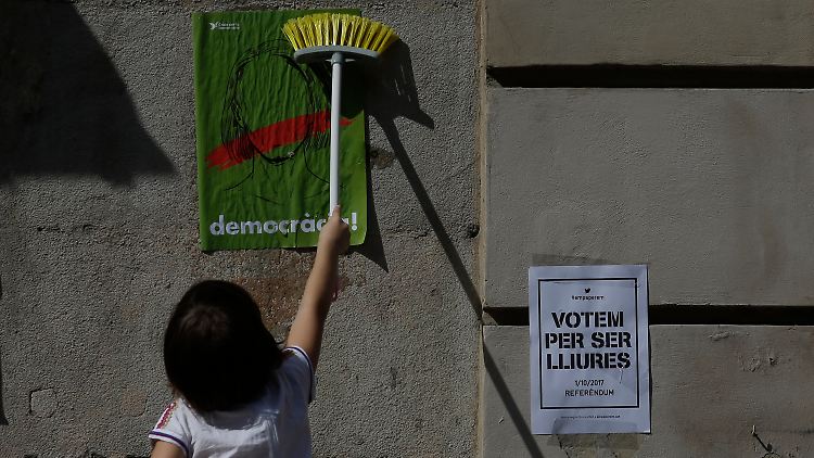 Ein junges Mädchen klebt in Barcelona einen Wahlaufruf an eine Häuserwand.