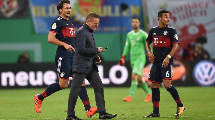 RB-Sportdirektor Ralf Rangnick eilt mit dem Handy in der Hand zum Schiedsrichter. Mats Hummels will ihn aufhalten.