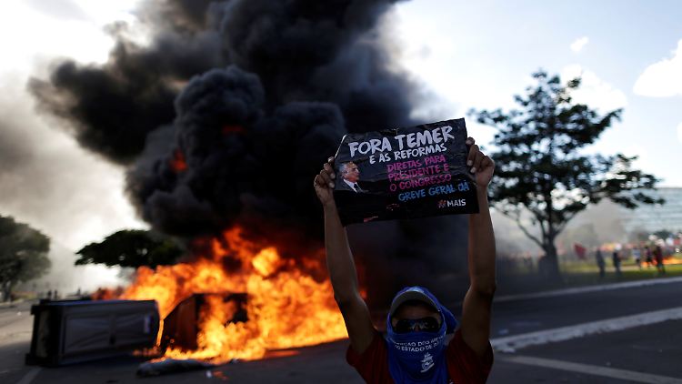 Vor einer brennenden Straßenblockade demonstriert ein Mann gegen den brasilianischen Präsidenten Michel Temer.
