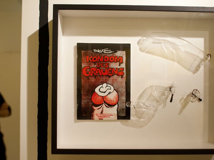 Original des Comiczeichners Ralf König mit dem Titel "Kondom des Grauens" neben Kondomen aus geblasenem Glas. Die Ausstellungsstücke waren Teil der Ausstellung "Superqueeroes".