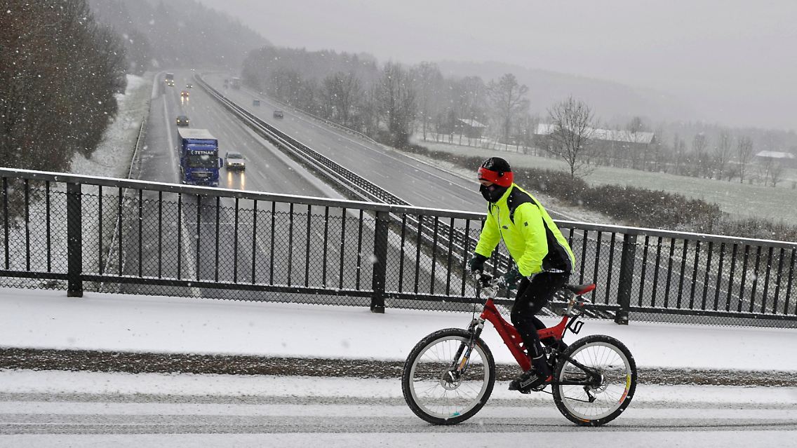 Trotz dichtem Schneefall und Temperaturen unter dem Gefrierpunkt fährt ein dick vermummter Mountainbiker am Irschenberg auf einer Autobahnbrücke der A8 München-Salzburg.