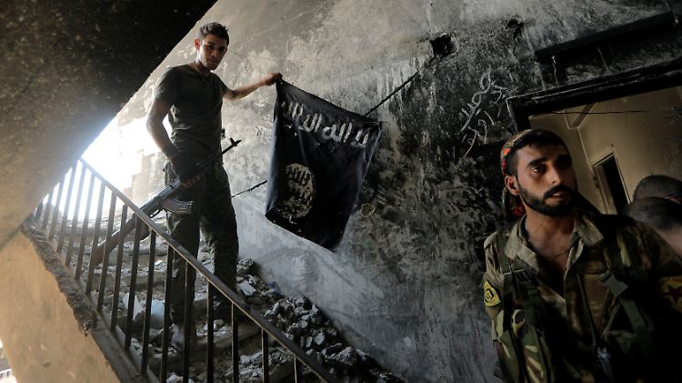 Zwei kurdische Kämpfer nehmen eine IS-Flagge von einer Wand in einem Gebäude der einstigen "Hauptstadt" des IS, Rakka.
