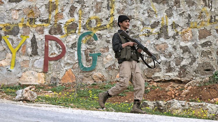 Von der Türkei unterstützte Rebellen präsentieren sich vor dem Schriftzug der kurdischen YPG in der Region Afrin. Die bekommt zusehends Unterstützung aus anderen Teilen des Landes.