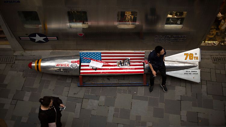 Ein Chinese sitzt in Peking auf auf einer Bank in Form einer Bombe mit US-Flagge, die als Werbemittel vor einem amerikanischen Bekleidungsgeschäft steht.