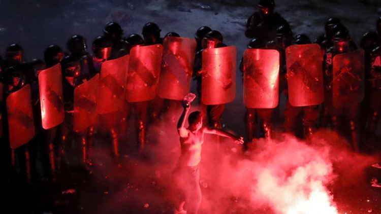 Ein Demonstrant wirft Steine auf eine in Position stehende Polizeieinheit. 
