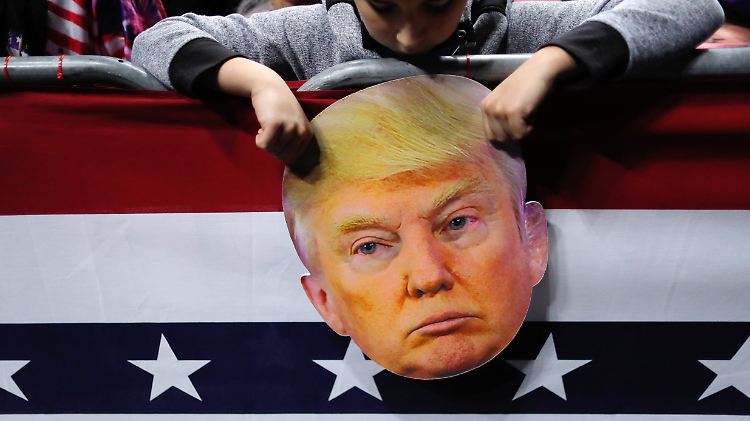 Ein Junge hält bei einer Wahlkampfveranstaltung einen Kopf aus Pappe von Donald Trump in den Händen.
