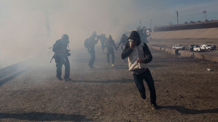 An der Grenze zu den USA versuchen sich Flüchtlinge vor dem Tränengas zu schützen.