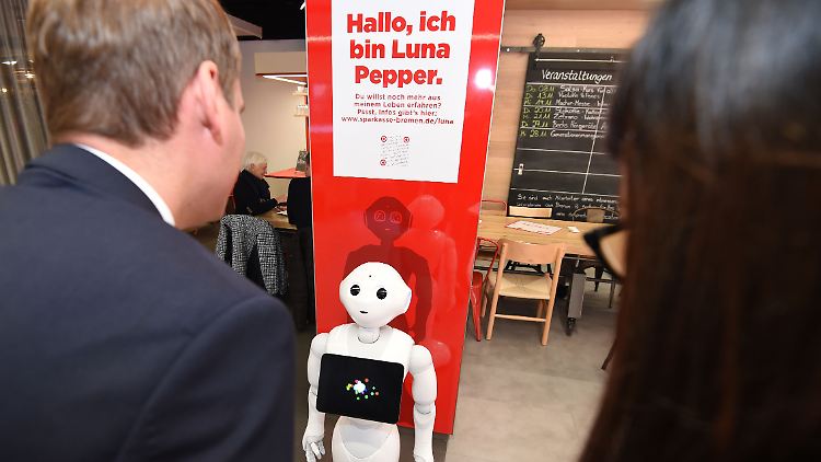Filialleiter Alexander Löde spricht in einer Bremer Sparkasse mit Roboter-Dame Luna Pepper.