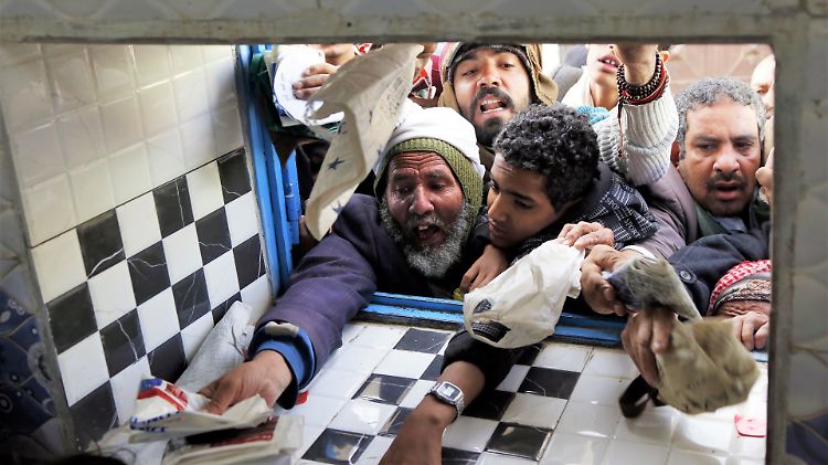 Menschen versammeln sich in Sanaa vor einem Fenster, um ihre täglichen Hilfsmittel von einem Lebensmittelverteilzentrum zu erhalten.