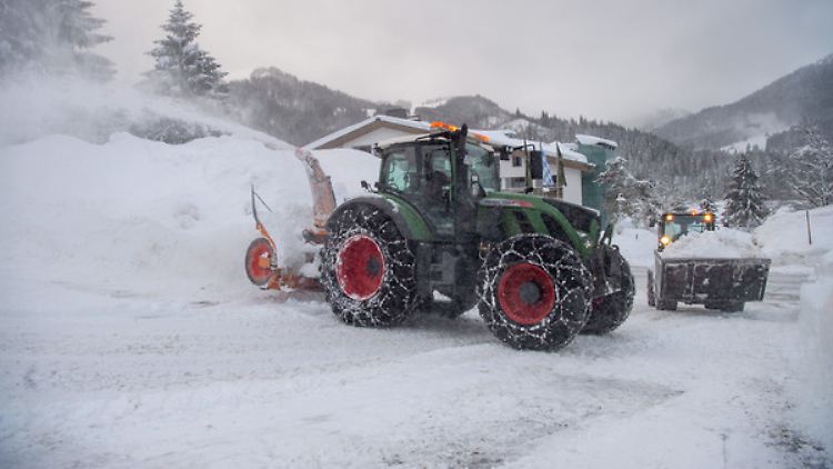 Eine Schneefräse und ein Radlader räumen in Bayern eine Straße. 