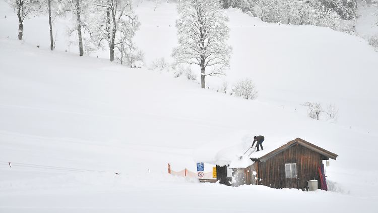 Ein Mann schaufelt Schnee vom Dach der Liftstation in Flachau, Österreich.