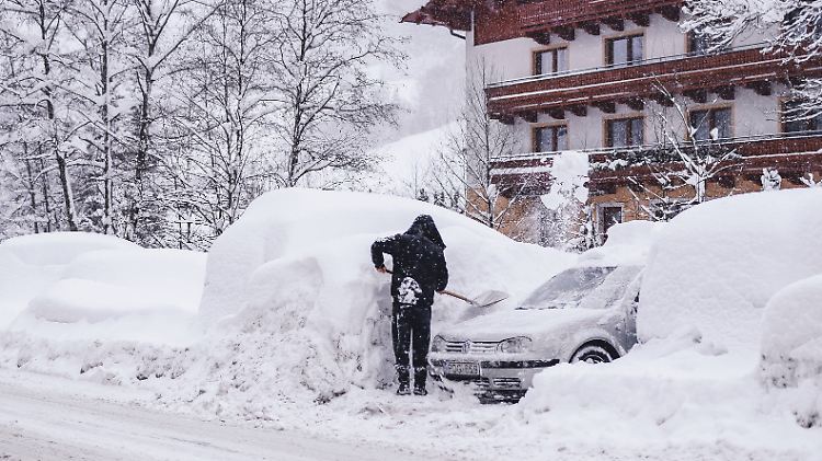 Ein Tourist versucht im österreichischen Saalbach sein Fahrzeug vom Schnee zu befreien.