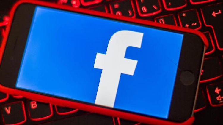Ein iPhone mit dem Logo von Facebook liegt auf der rot beleuchteten Tastatur eines Laptops. Foto: Lino Mirgeler/Archivbild