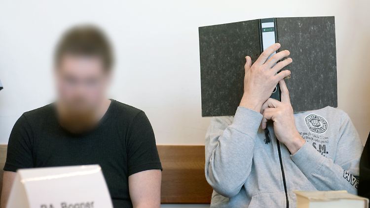 Einer der Angeklagten versteckt zum Prozessauftakt sein Gesicht hinter einem Aktenordner. 