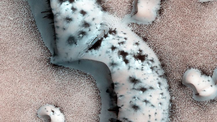 Polare Eiskappen auf dem Mars sind eine Kombination aus Wassereis und gefrorenem CO2. Wie seine gasförmige Form lässt gefrorenes CO2 Sonnenlicht eindringen, während es Wärme speichert. Im Sommer erzeugt dieser Festkörper-Treibhauseffekt unter dem Eis Wärmestau, hier als schwarze Punkte im Eis.