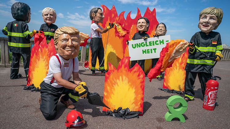 Demonstranten in Biarritz tragen Masken von Trump und Merkel: Die Kanzlerin und der US-Präsident werden sich am Rande des G7-Gipfels auch zum Vier-Augen-Gespräch treffen.