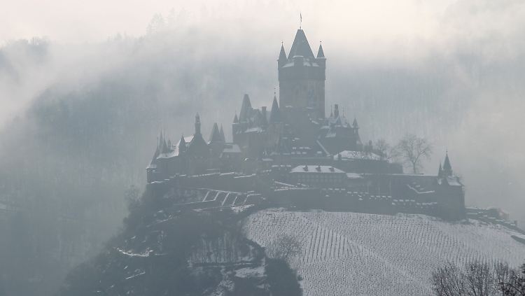Die verschneite Reichsburg hoch über der Stadt Cochem ist in Nebelschwaden gehüllt.