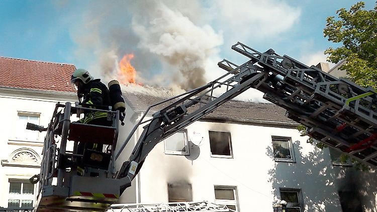 Aus dem Dachstuhl des Mehrfamilienhauses schlagen hohe Flammen.